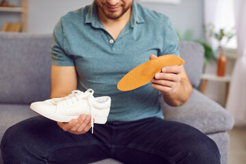 Man putting new orthopedic insole into sport shoe, white sneaker for walking, running. Foot care,...