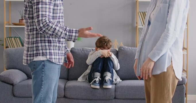 Stressed upset boy kid sitting on sofa while his parents having fighting or quarrel conflict arguing at home. Divorce and domestic problem in family concept. 4k video. Slow motion video.