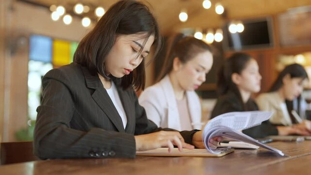 A woman is reading a book at a table with other women. Scene is focused and studious