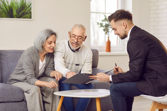 Elderly couple is carefully studying documents provided by financial advisor in cozy living room. Smiling mature family discussing retirement planning, property arrangements or investment choices.