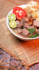 Close up Clear beef soup with potatoes, tomatoes, lime slices, and fried shallots. Served on a bowl white with Bamboo mat and burlap