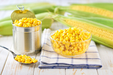Canned sweet corn kernels in a transparent bowl on a white table, selective focus.