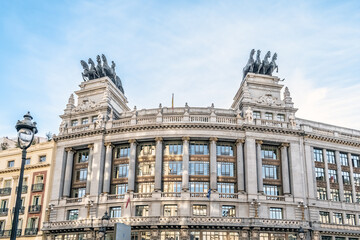 Facade of the historic Banco de Bilbao building in Madrid showcasing its classical architectural elements and and iconic chariots on the rooftop. Madrid, Spain - November 30, 2021