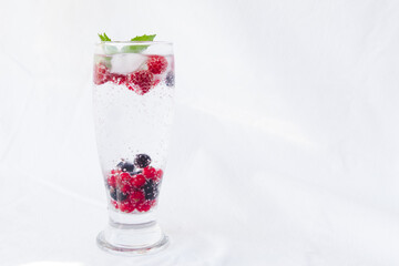 Carbonated drinks with fresh berries and ice. Fresh cold sparkling bubble water with mint, raspberry, black and red currant in transparent glass with ice, angle view macro. Food and drink concept
