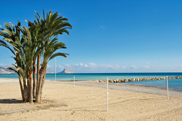 Beautiful white pebble beach with beach volleyball net in Altea. View from Altea to turquoise Mediterranean sea, Calpe city and Rock of Ifach. Altea, Alicante province, Spain