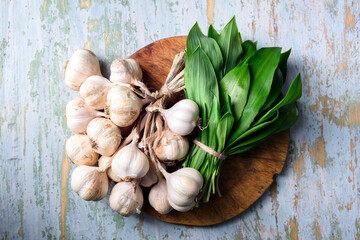 Garlic heads and fresh bear's wild garlic leaves on wooden cutting board close up. Food photography, top view