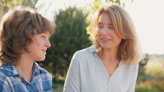 Warm moment of Caucasian mother talking with her little son. Parent spending free time with beloved child. People enjoying warm sunshine in summer. Smiling during cheerful conversation.