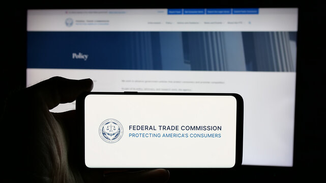 Stuttgart, Germany - 01-24-2025: Person holding cellphone with logo of US government agency Federal Trade Commission (FTC) on screen in front of webpage. Focus on phone display.