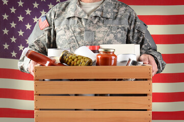 Closeup of a soldier in fatigues holding a wooden box full of canned and packaged food for a holiday charity drive