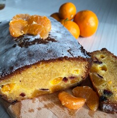 Freshly baked citrus loaf cake with tangerine slices, cranberries, and glaze, served on a wooden board with whole tangerines, showcasing rustic charm festive flavor, concept of baking, dessert
