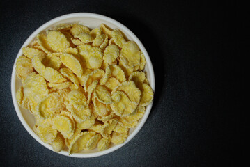 crispy corn flakes glazed with sugar in a porcelain bowl on a black background
