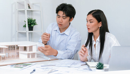 Professional male asian architect using ruler to measure house model length while young beautiful...