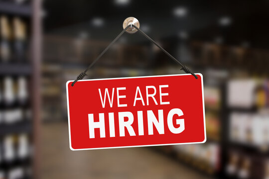 Red sign hanging at the glass door of a shop saying: "We are Hiring".