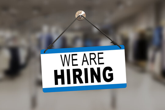 Red sign hanging at the glass door of a shop saying: "We are Hiring".