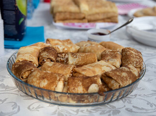 Glass dish filled with rolled pancakes on a table, with jam and other food items in a casual dining setting, showcasing comfort and culinary delight, concept of breakfast, home dining, lifestyle
