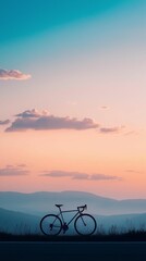 Fototapeta premium A lone road bike outlined against a gradient sky, framed by soft clouds and distant hills, evoking a sense of quiet adventure