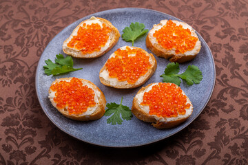 Canapes with red caviar on a plate decorated with cilantro on a brown tablecloth