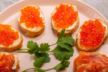 Canapes with red caviar and salted salmon on a plate decorated with cilantro