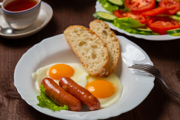 Breakfast two plates fried eggs with sausages white bread and tea in cups