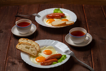Breakfast two plates fried eggs with sausages white bread and tea in cups