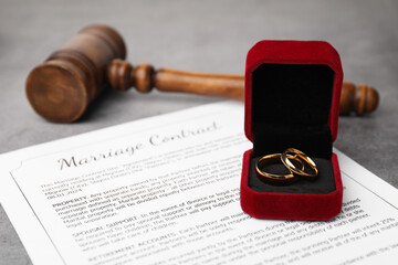 Marriage contract, gavel and golden rings on grey table, closeup