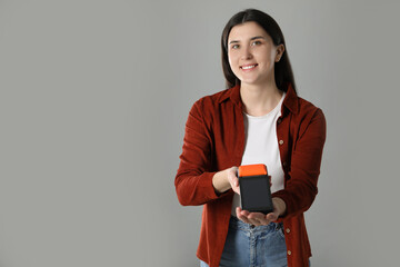 Naklejka premium Happy young woman with payment terminal on gray background, space for text