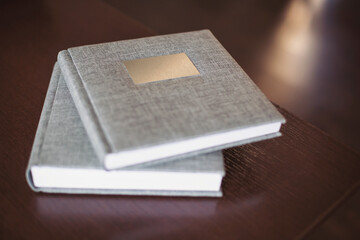 Two gray fabric wedding photo album with engraving on the cover lie on a wooden table. Soft focus. Memory book. Family photos archive saved in brightly designed photo book.
