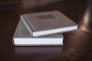 Two gray fabric wedding photo album with engraving on the cover lie on a wooden table. Soft focus. Memory book. Family photos archive saved in brightly designed photo book.