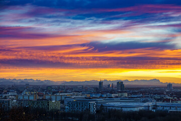 Skyline of Munich, Bavaria, Germany with view of the snow-capped Alps against a colorful sunset sky with dramatic clouds