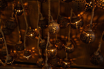 Handcrafted hanging lanterns made from natural materials with intricate perforated patterns. Warm glowing light creates decorative shadows on the wooden background, perfect for ambient designs.