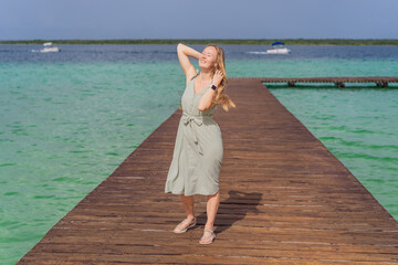 Female tourist in a turquoise dress standing on a wooden pier over the turquoise waters of Bacalar...