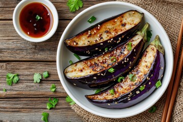 Gaji Namul a Korean side dish of steamed seasoned eggplant in a white bowl with soy sauce and chopsticks displayed on a wooden table from a top down perspective