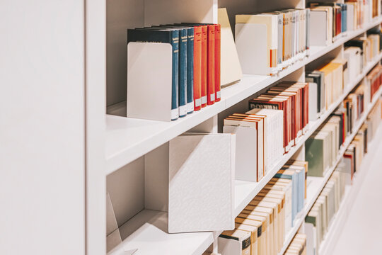 Colorful book spines on shelves in library with warm lighting. Concept of knowledge, cultural enrichment - Powered by Adobe
