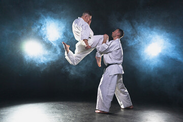 Martial arts masters on dark background. Strong man fighters in white kimono for karate martial arts fighting training in black gym. Karate fighters training punches kicks practicing fight sparring © Юлия Завалишина