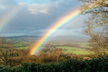 A majestic rainbow stretches across a lush green countryside, illuminating the landscape after a spring rain. The scenery reflects fresh foliage and distant hills, evoking tranquility
