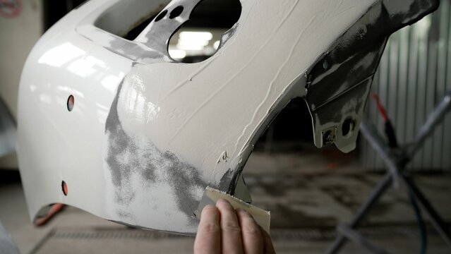 Professional automotive technician repairing white car bumper, carefully filling dents and smoothing surface using specialized body repair techniques - Powered by Adobe