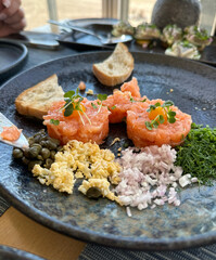 Elegant salmon tartare served with capers, chopped dill, onions, egg crumble, and microgreens on a dark ceramic plate, showcasing gourmet, concept of fine dining, culinary artistry, lifestyle