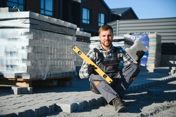 Builder laying a paving brick placing it on the sand foundation with gloved hands