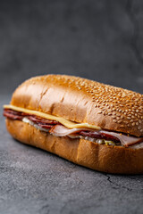 Sesame seed baguette filled with layers of smoked meats, cheese, and fresh spreads on a rustic stone background