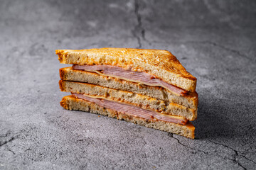 Classic grilled ham and cheese sandwich with golden toasted bread, stacked neatly on a rustic stone surface