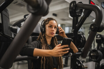 young woman with headphones use mobile phone and take a break at gym