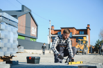 Construction worker installing and laying pavement stones on terrace, road or sidewalk. Worker using stones and rubber hammer to build stone sidewalk