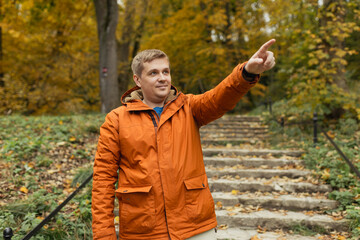 Obraz premium Blonde male with backpack pointing finger outdoors, he hiking on woodland. Active lifestyle concept. Trip, travel and people banner. High quality photo