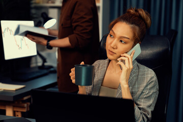Businesswoman calling with customers to make new project job at modern office while coworker checking paperwork folder of business plan to database report meeting at over late night time. Infobahn.
