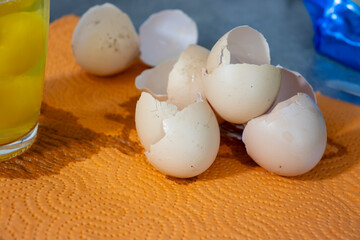 A close-up of cracked eggshells scattered on an orange paper towel, with a glass of egg yolk in the background, evoking freshness and culinary creativity.
