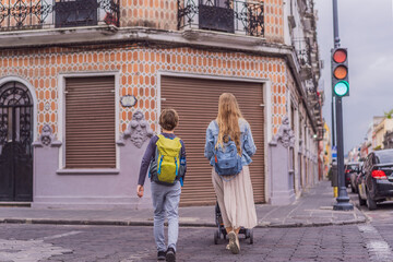 Fototapeta premium Mother tourist with her toddler and teenage sons walking through the colorful colonial streets of Puebla, Mexico. Travel, cultural exploration, and vibrant architecture concept