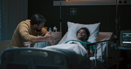 Young girl lies unconscious in a hospital bed with an oxygen tube in her nose. Beside her sits a tired-looking man.