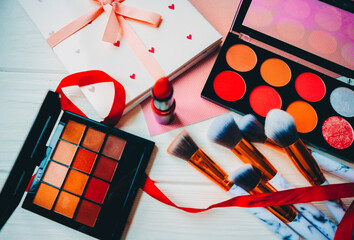 Makeup brushes, lipstick, notepad and eye shadow palette on a white wooden background