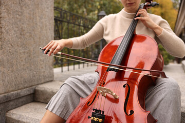 Fototapeta premium Young woman playing cello on stairs outdoors, closeup. Classic musical instrument