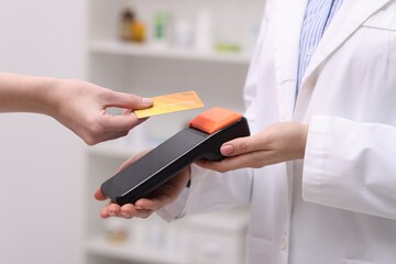 Woman paying with credit card via terminal against blurred background, closeup